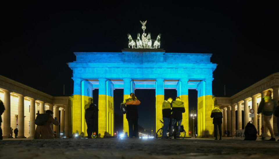 People look at the Brandenburg Gate after it was illuminated in the colours of the Ukrainian flag to show solidarity with the country during the tensions with Russia in Berlin, Germany, Wednesday, Feb. 23, 2022. (AP Photo/Markus Schreiber)